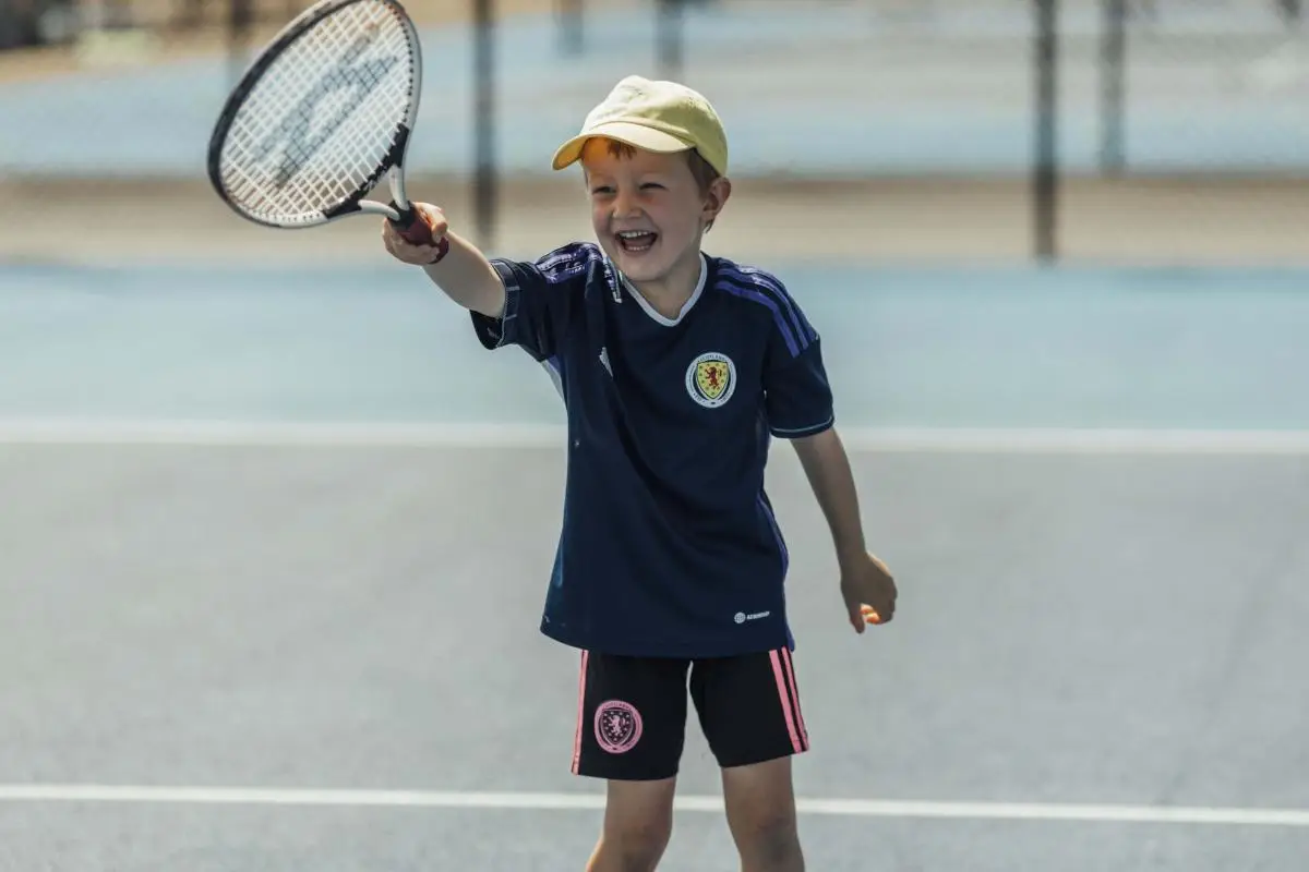 school child learning to play tennis